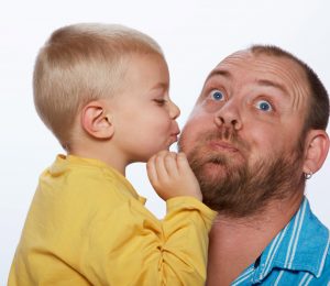 Little blond boy gives his father a kiss on isolated studio background
